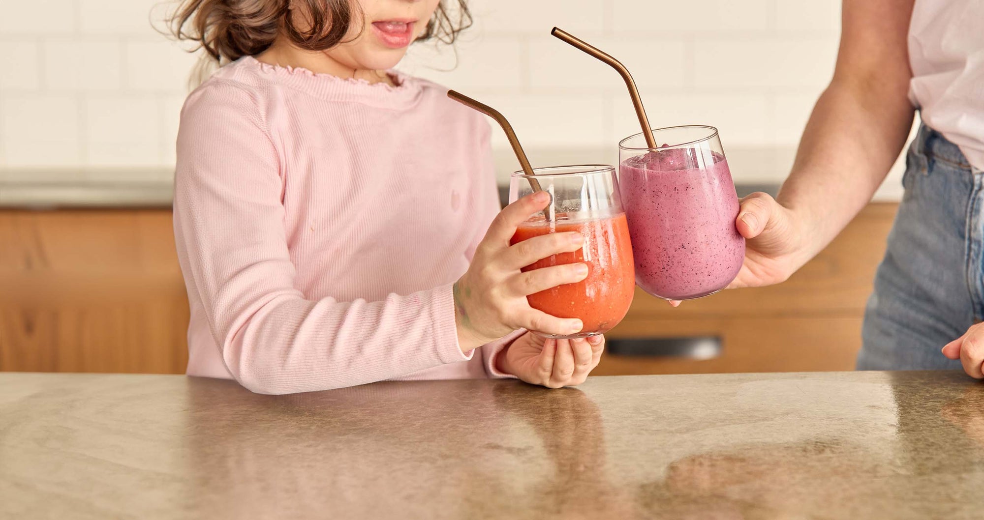 Parent and child cheers with smoothies in kitchen at home