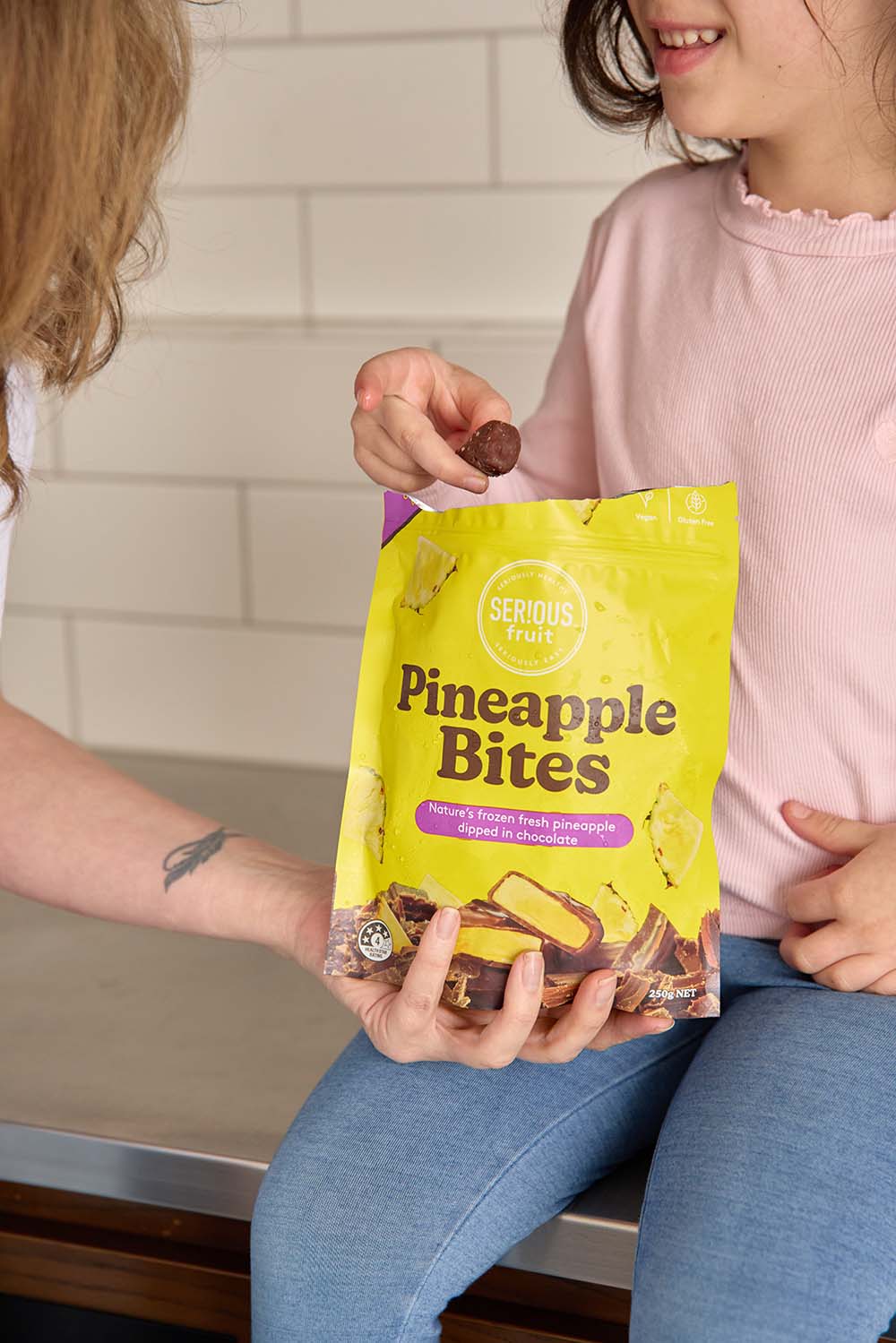 Child taking frozen pineapple bite out of the pack sitting on kitchen bench